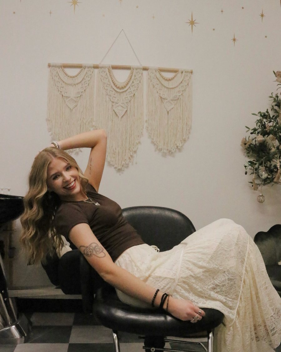 Kayla MacArthur smiling in her Sola Salon studio in Auburn, CA — long blonde hair, mirror and shelves behind her.